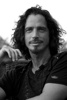 a black and white photo of a man with long curly hair sitting in a chair