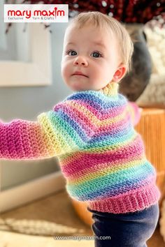 a baby wearing a multicolored knitted sweater and holding onto the arm of someone's hand