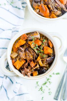 two bowls filled with meat and vegetables on top of a white table next to silverware