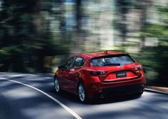 the rear end of a red mazda hatchback driving on a road with blurry trees in the background