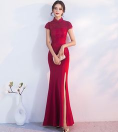 a woman in a long red dress standing next to a white vase with flowers on it