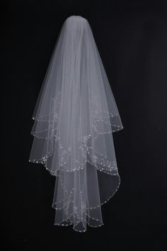 a white veil hanging from the side of a black wall with beaded trim on it