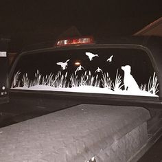 the dog is sitting in the grass behind the truck's rear window at night