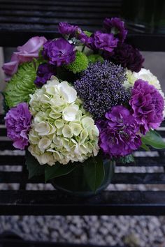 purple and white flowers in a vase on a bench