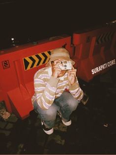 a man sitting in front of a red dumpster taking a photo with his camera