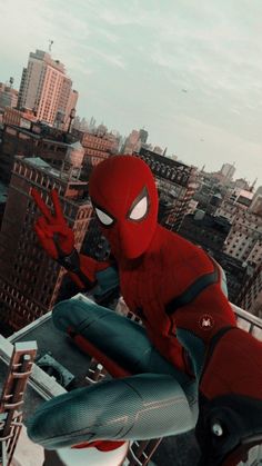 the spider - man is sitting on top of a building with his hands in the air