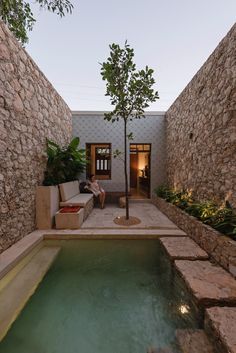 a person sitting on a couch next to a tree near a pool in a courtyard