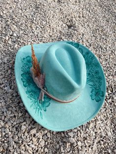 This is a hand burned cowboy hat with details of flowers and foliage. To go with it is has an light pink felt ribbon tied with a brown leather strip of fabric. It is turquoise and it burned to this beautiful dark green/turquoise color.  These custom hand burned wide brim western hats have a unique to the hat fabric hand tied band with feathers and other add ins to make the hat one of a kind. Every hat is customizable free of charge so please feel free to reach out with any customization question and we can make the hat your own!  Hat Details: It is a Cattleman Cowboy Hat in vegan suede. Classic cattleman crown shape. Brim is slightly upturned on the sides. Crown size: 57 cm. Adjustable sizing, hook-and-loop tab inside sweatband. Please allow up to 2 weeks to receive your hat! Teal Cowgirl Hat, Western Green Hat Band For Festivals, Western Green Hat Bands For Festival, Green Western Style Hat Band For Festivals, Western Green Hat For Country Events, Turquoise Wide Brim Hat For Kentucky Derby, Green Western Hat Bands For Kentucky Derby, Western Green Hat Bands For Kentucky Derby, Turquoise Hats For Kentucky Derby And Festivals