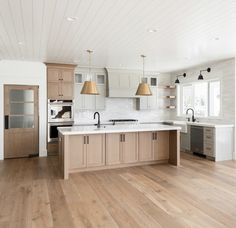 a large kitchen with wooden floors and white walls, two pendant lights over the island