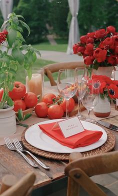 a table set with red flowers and place settings for an outdoor dinner or brunch