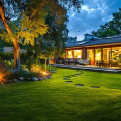 the backyard is lit up at night with lights shining on the grass and stepping stones