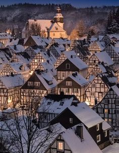 a town with lots of houses covered in snow at night, lit up by street lights