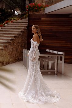 a woman in a wedding dress is standing on the floor next to some stairs and flowers