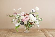 a vase filled with white and pink flowers on top of a wooden table next to a wall