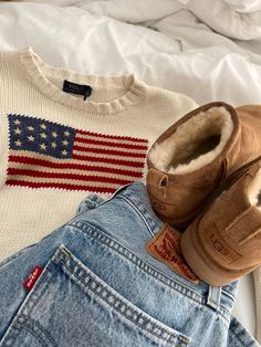 an american flag sweater, jeans and shoes are on the bed next to a pair of slippers