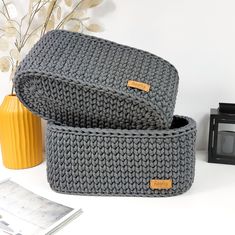 two knitted storage baskets sitting next to each other on a white table with a yellow vase