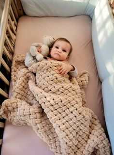 a baby laying in a crocheted bed with a teddy bear on it's back