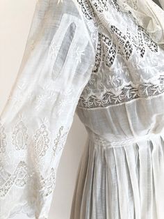 "Antique Edwardian white cotton lawn dress has eyelet lace embroidery throughout the bodice, sleeves, and around the hem. The dress has a ruffle trimmed net collar and net under bodice that has a crossover snap detail. The dress has snap and hook and eye closures at the skirt and bodice. Condition Overall excellent. There's a repair to the right sleeve, and orange stains near the seam. The front skirt has stains at the hem, the back skirt has some stains near the top of the lace, and yellowing a White Lace Dress With Broderie Anglaise, White Lace Dress With Lace Cuffs For Spring, White Spring Dress With Ruffled Collar, White Cotton Dress With Ruffled Collar, White Dress With Ruffled Collar For Spring, Classic Broderie Anglaise Dresses, White Dresses With Ruffled Collar For Spring, White Lace Dress With Lace Collar For Summer, White Summer Dress With Lace Cuffs