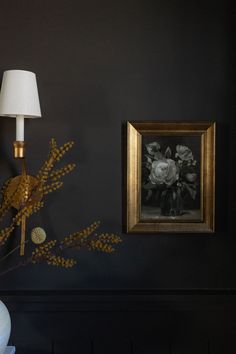 a vase with flowers is sitting next to a painting on the wall and a lamp