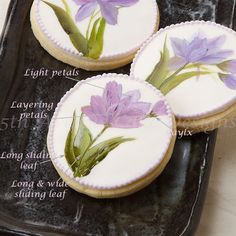 three decorated cookies with flowers on them sitting on a black platter next to a white tablecloth