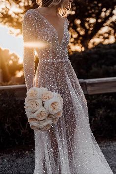 a woman in a wedding dress with flowers on her hand and the sun shining behind her