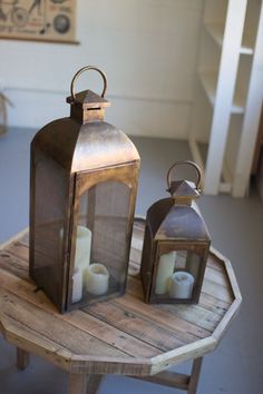 two metal lanterns sitting on top of a wooden table next to each other with candles in them