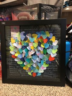 a black frame filled with lots of different colored paper heart shaped items on top of a table