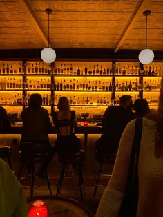 people sitting at tables in front of a bar with liquor bottles on the wall behind them