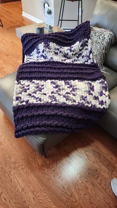 a purple and white crocheted blanket sitting on top of a gray couch in a living room