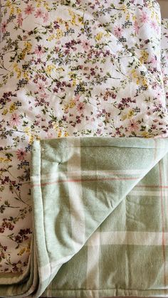 an unmade bed with flowers on it and a blanket folded up in front of it