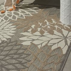 an area rug with flowers on it and a vase next to it in the background