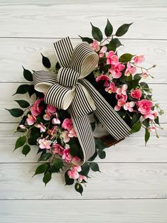 a wreath with pink flowers and green leaves on a white wooden background is tied with a black ribbon