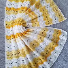 a yellow and white crocheted blanket on top of a bed next to a pillow