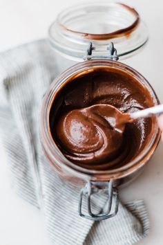 a jar filled with chocolate frosting sitting on top of a table next to a napkin