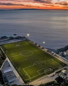 an aerial view of a soccer field at night with the sun setting over the water