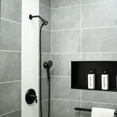 a black and white photo of a bathroom with gray tiles on the walls, toilet paper holders in the shower