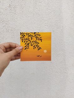 a person holding up a piece of paper with trees and birds painted on it in front of a white wall