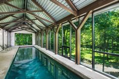 an indoor swimming pool surrounded by glass walls and wood framed windows that overlook the trees