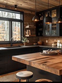 a kitchen with black cabinets and wooden counter tops in front of a large window that looks out onto the woods