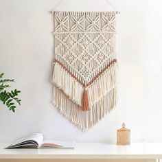 a macrame hanging on the wall next to a book and potted plant