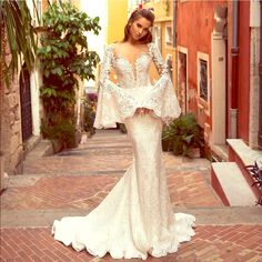 a woman in a white wedding dress standing on a brick walkway with her arms behind her back