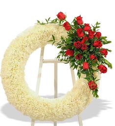 a white wreath with red roses and greenery on it is placed in front of a white backdrop