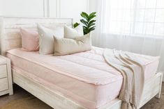 a bed with pink sheets and pillows in a bedroom next to a white dresser holding a potted plant