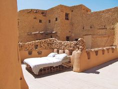 a bed sitting on top of a wooden floor next to a stone wall and building