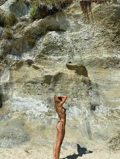 a woman standing on top of a sandy beach next to a rocky cliff and water