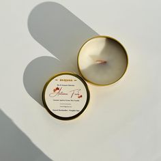 a white candle in a metal container with a label on the lid next to it