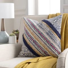 a white couch with yellow throw pillows and a blue vase on the table next to it