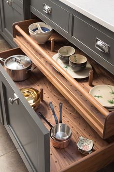 an open drawer in a kitchen with bowls and pans on the bottom shelf next to it