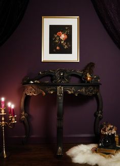 an ornate console table with candles in front of a purple wall and painting on the wall