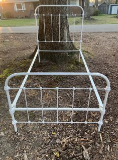 a white metal bed frame next to a tree